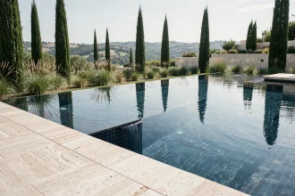 Piscine à débordement moderne avec carrelage bleu nuit intégrée dans un jardin contemporain avec vue panoramique sur la campagne