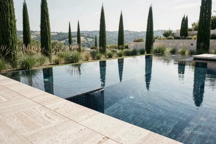 Piscine à débordement moderne avec carrelage bleu nuit intégrée dans un jardin contemporain avec vue panoramique sur la campagne